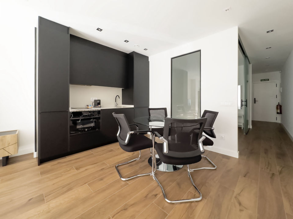 Cocina moderna en los apartamentos de lujo Alfisa, en color negro con la mesa y sillas a juego, equipada con horno, vitrocerámica, cafetera y mesa de comedor con sillas. La nevera está integrada y oculta. También se aprecia el sistema de aire acondicionado, en un espacio con diseño contemporáneo.