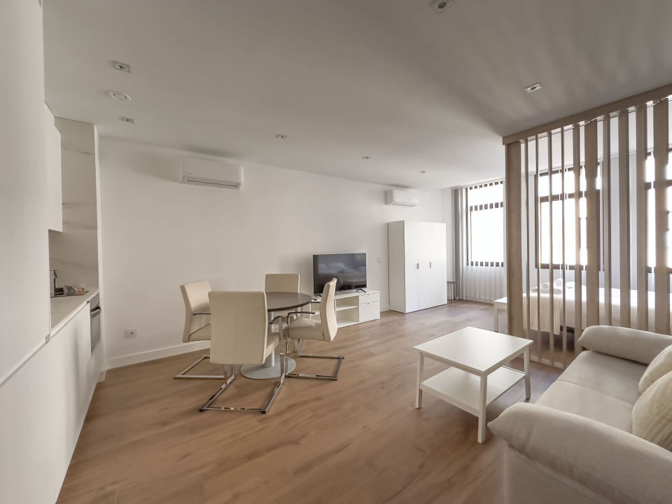 vista general del apartamento de lujo B3 de Alfisa, situado en l calle príncipe 5, a seis minutos a pie de la Puerta del Sol, se ve una cama con separación del resto de la estancia donde en un mismo espacio se sitúan el sofá cama, una mesa comedor con cuatro sillas, un mueble moderno bajo con televisor