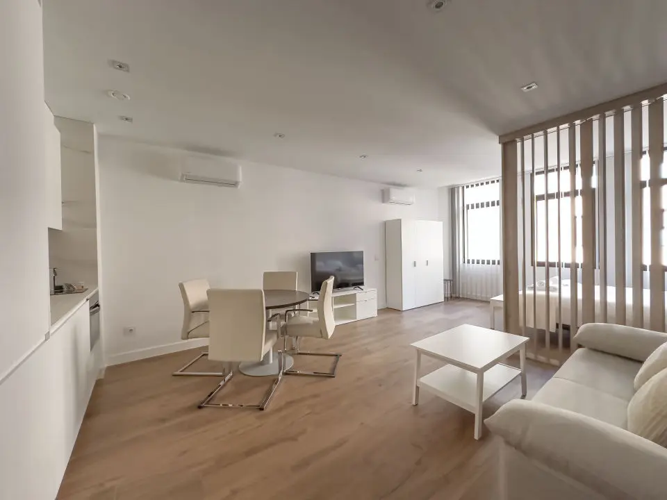 vista general del apartamento de lujo B3 de Alfisa, situado en l calle príncipe 5, a seis minutos a pie de la Puerta del Sol, se ve una cama con separación del resto de la estancia donde en un mismo espacio se sitúan el sofá cama, una mesa comedor con cuatro sillas, un mueble moderno bajo con televisor